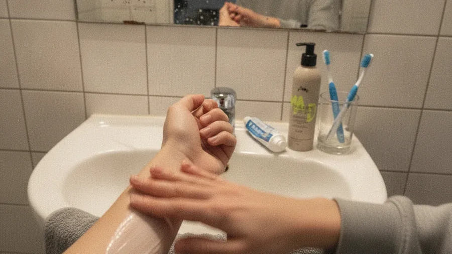 Clémence applique un émollient sur son avant-bras dans sa salle de bain