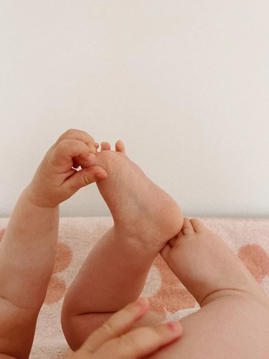 Un bébé attrape son pied, allongé sur sa table à langer